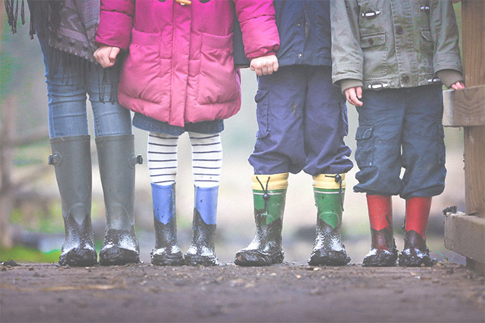 Four kids standing in a row on a bridge with muddy rain boots